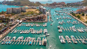 A marina with numerous boats docked, surrounded by buildings and a mountainous backdrop. - Marina View Open Studio Suite on Marina 645SF walk everywhere! NEW Rooftop Pool (Cabo San Lucas)