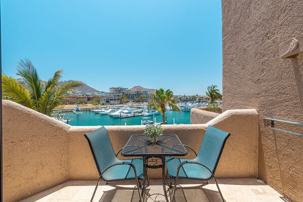 A balcony with a table and chairs overlooking a marina with boats and palm trees.