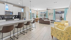 Una cocina moderna con una isla central, taburetes de bar y una zona de comedor con sofá y sillas.