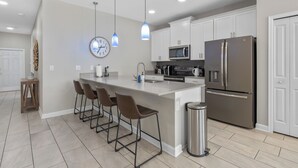 Una cocina moderna con una isla central, taburetes de bar, un refrigerador de acero inoxidable y un microondas.