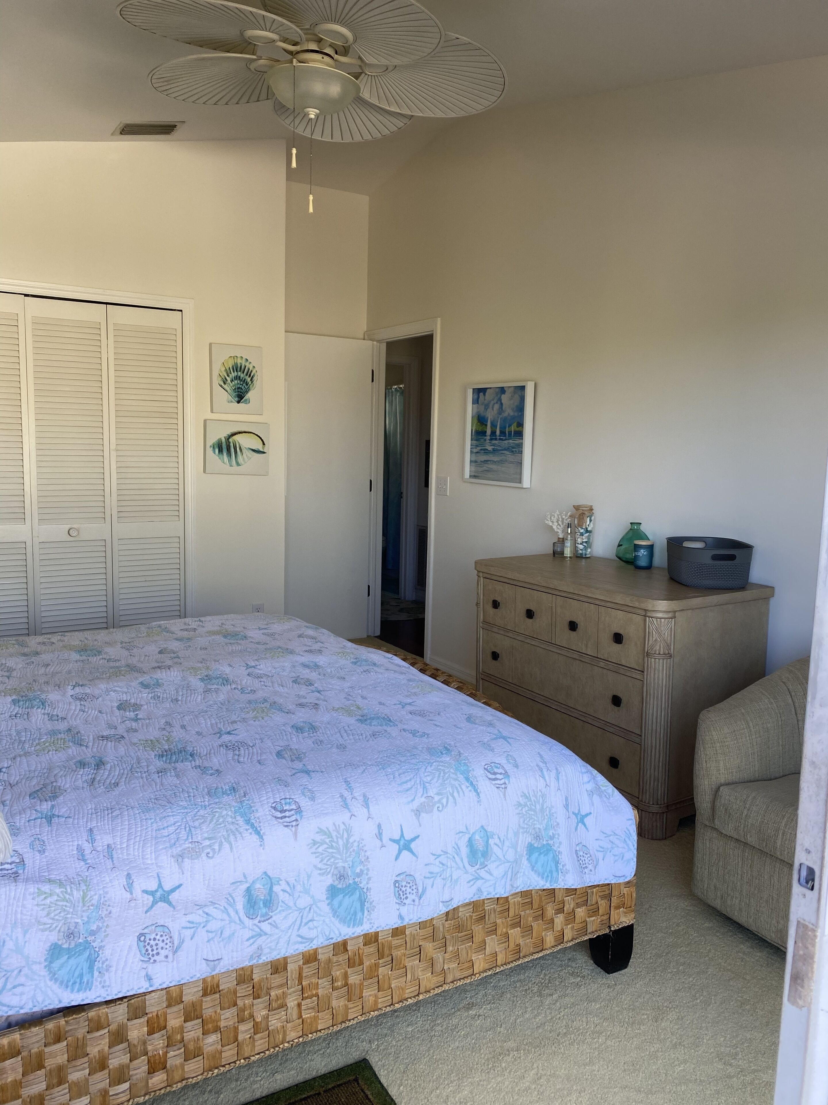 A bedroom with a bed, a dresser, a ceiling fan, and a door leading to another room.