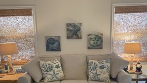 A living room with a beige sofa, decorative pillows, a glass coffee table, and wall art.