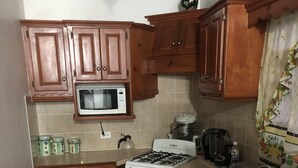 A compact kitchen with wooden cabinets, a microwave, a stove, and a sink.