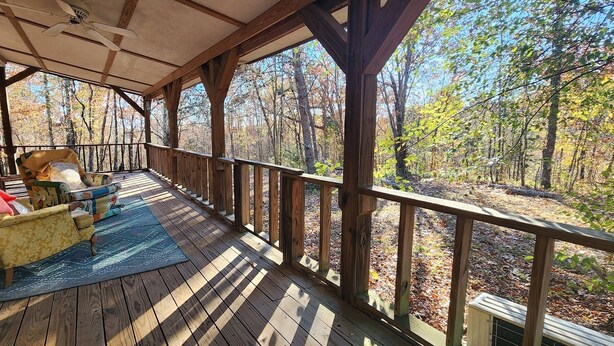 Terraza de madera con un sofá y una silla, con vista a un área boscosa.