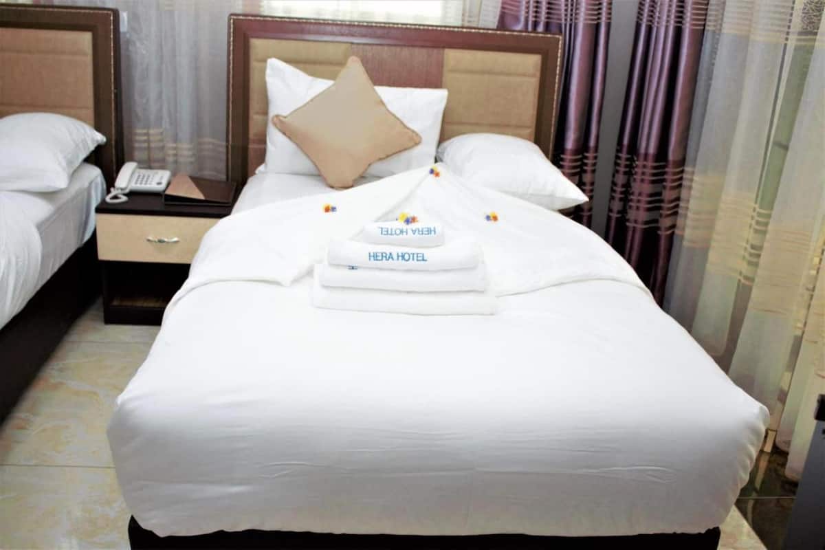 A hotel room with a neatly made bed, a bedside telephone, and a folded towel with the hotel name.