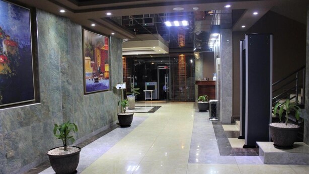 A hotel lobby with a marble floor, large paintings on the walls, and potted plants. - Hera Hotel (Kampala)