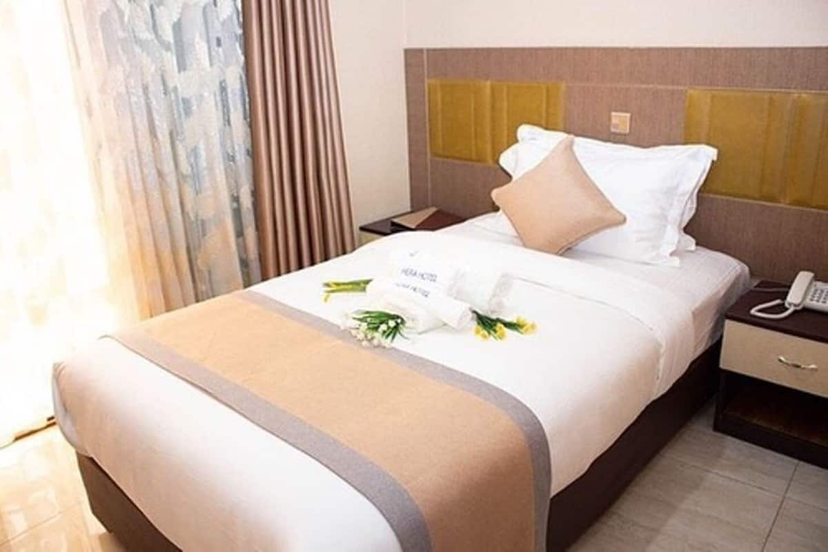 A neatly made hotel bed with a white and beige bedspread, a bouquet of flowers, and a bedside phone.
