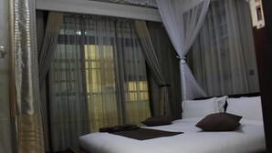 A hotel room with a large bed, white bedding, and sheer curtains. - Hera Hotel (Kampala)