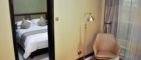 Una habitación de hotel con cama, una silla, una mesa y una lámpara de pie.