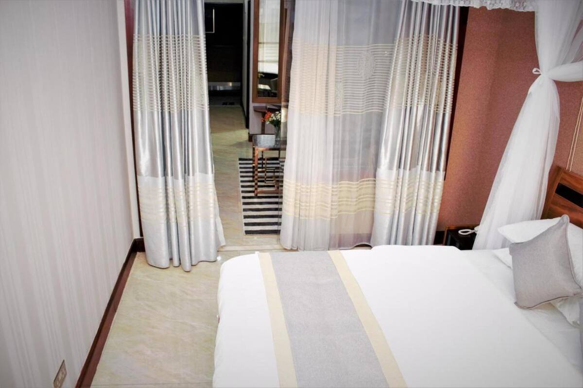 A hotel room with a bed, curtains, and a view of the hallway.