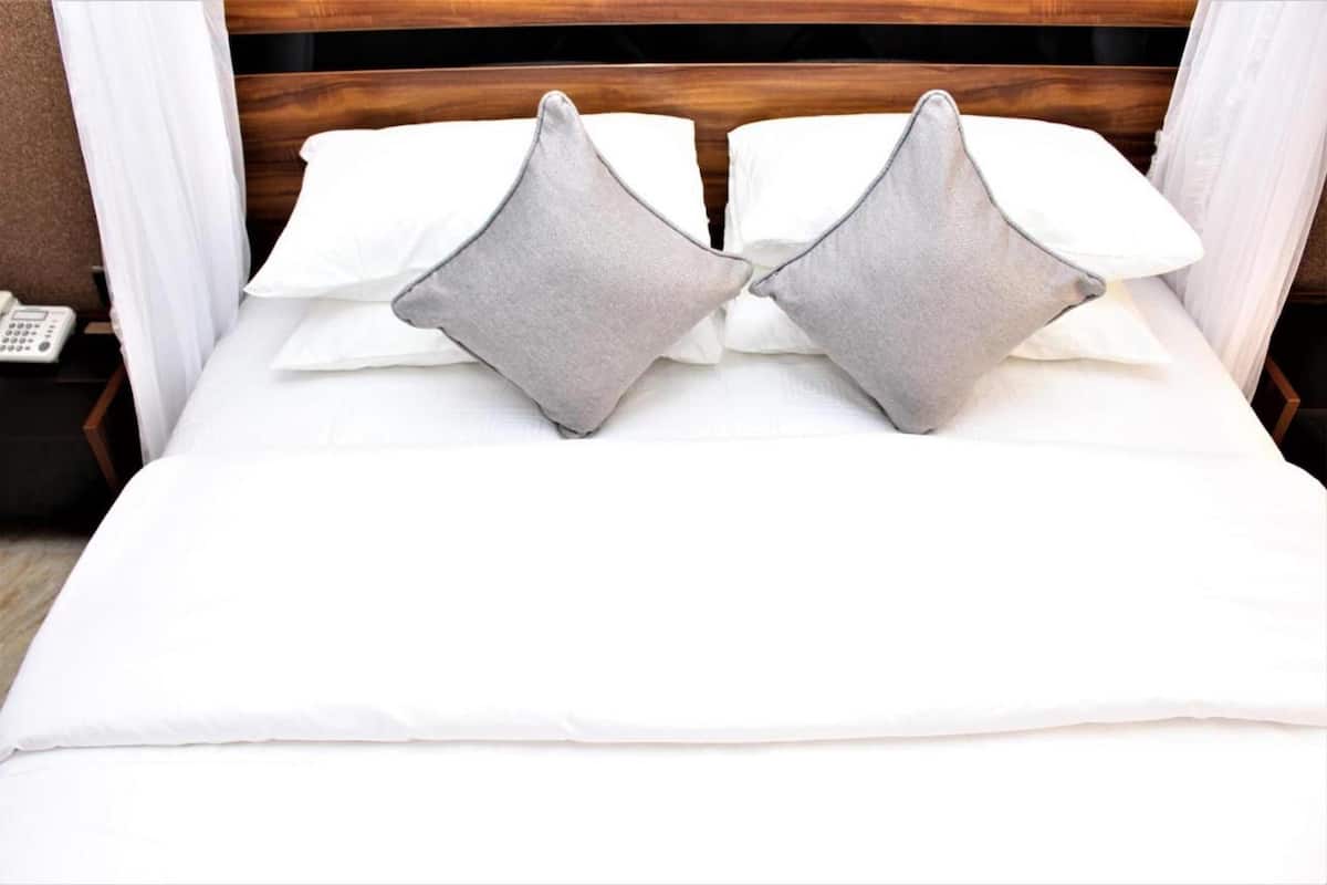 A neatly made bed with white linens and two grey pillows.