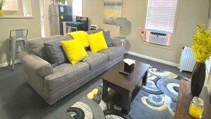 Ein Wohnzimmer mit grauem Sofa, gelben Kissen, einem Couchtisch und einem gemusterten Teppich.