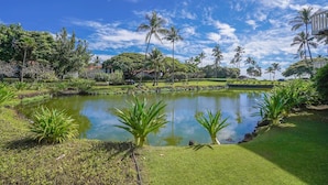 A serene garden with a pond, palm trees, and a building in the background. - Luxury Upgraded Condo #98, AC, Poipu Beach, Partial Ocean View (Koloa)