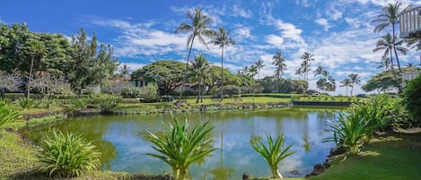A serene garden with a pond, palm trees, and a building in the background.