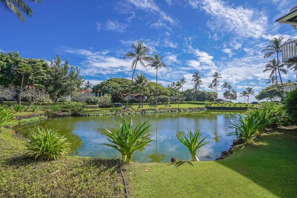 A serene garden with a pond, palm trees, and a building in the background.