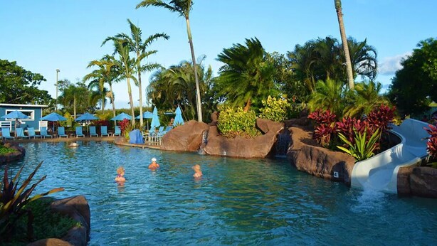 A pool area with lounge chairs, palm trees, and a water slide. - Luxury Upgraded Condo #98, AC, Poipu Beach, Partial Ocean View (Koloa)