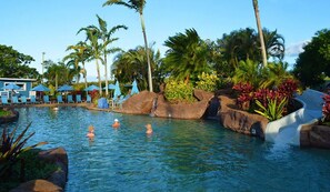 A pool area with lounge chairs, palm trees, and a water slide. - Luxury Upgraded Condo #98, AC, Poipu Beach, Partial Ocean View (Koloa)