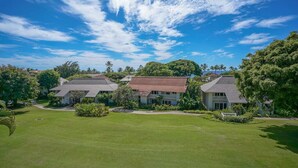 A residential area with three houses, each with a distinct roof style, surrounded by well-maintained lawns and trees. - Luxury Upgraded Condo #98, AC, Poipu Beach, Partial Ocean View (Koloa)