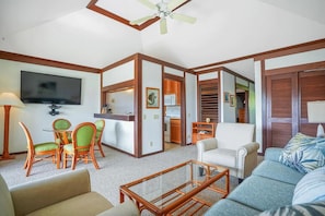 Sala de estar com televisão, cadeiras verdes, sofá branco e ventilador de teto.