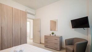 Un dormitorio con cama, cómoda, silla, televisor y armario.