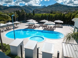 Una piscina con sillas de descanso y sombrillas, rodeada de montañas y vegetación.