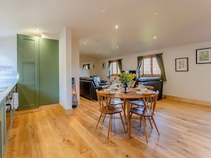 A modern kitchen with wooden flooring, a dining area with a table set for four, and a living area with a sofa and a TV.