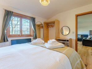 Une chambre d’hôtel dotée d’un grand lit, d’une coiffeuse avec un miroir, d’un coin salon avec un canapé et offrant une vue sur les arbres par la fenêtre.