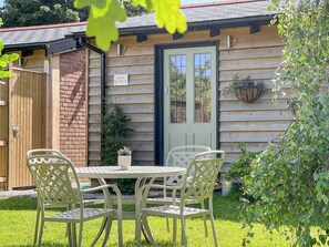 A wooden cottage with a green door, a sign reading "Bluebell Lodge," and a small table with chairs in the front yard.