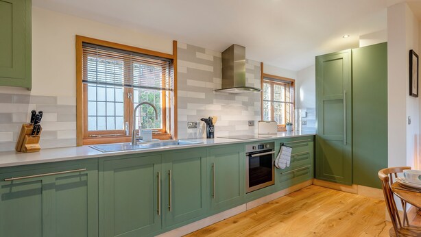 A kitchen with green cabinets, wooden flooring, a built-in oven, and a window with blinds. - Bluebell Lodge-UK32958 (Ashford)