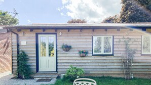A wooden house with a front door, two windows, and a small garden with a table and chairs. - Bluebell Lodge-UK32958 (Ashford)