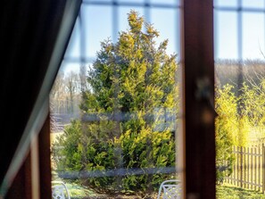 Une vue à travers une fenêtre sur un jardin avec une clôture en bois et une chaise blanche.
