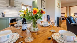 A dining table set with plates, bowls, cutlery, and a wine bottle, surrounded by a vase of flowers. - Bluebell Lodge-UK32958 (Ashford)