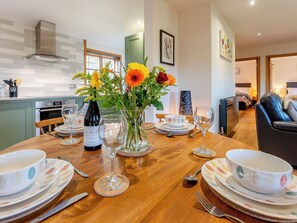 A dining table set with plates, bowls, cutlery, and a wine bottle, surrounded by a vase of flowers. - Bluebell Lodge-UK32958 (Ashford)