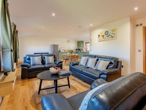 A modern living room with two black leather sofas, a wooden coffee table, and a dining area in the background.