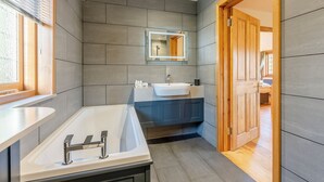 A modern bathroom with a large bathtub, a sink, and a mirror. - Bluebell Lodge-UK32958 (Ashford)