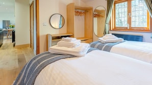 A hotel room with two beds, a desk, a mirror, and a window with curtains. - Bluebell Lodge-UK32958 (Ashford)