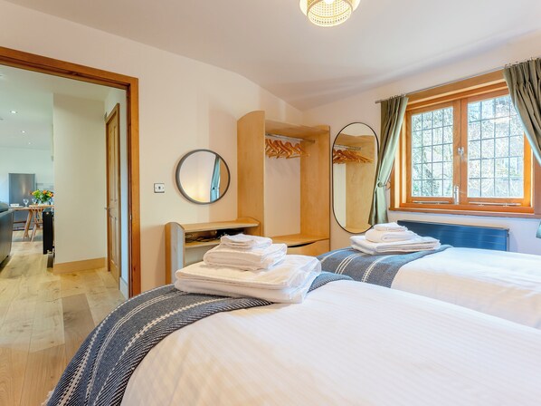 A hotel room with two beds, a desk, a mirror, and a window with curtains.