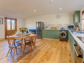 A modern kitchen with a dining area, wooden flooring, and green cabinets.