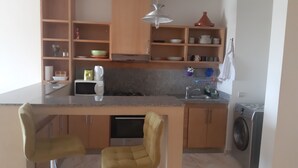 A compact kitchen with a microwave, sink, and a washing machine. There are wooden cabinets and a small dining area with two chairs. - AIRPORT to Comme à la maison 2, 5 minutes from the airport (Nouaceur)