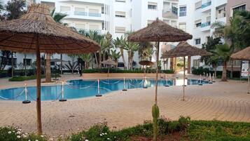A swimming pool area with thatched umbrellas, palm trees, and a brick pathway.