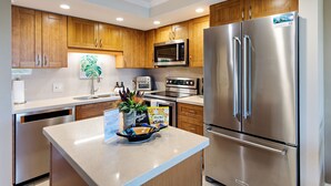 A modern kitchen with wooden cabinets, stainless steel appliances, and a central island with a decorative bowl. - Remodeled 1BD/2BA in Best South Kihei Location, split A/C, 3 min from the beach! (Kihei)