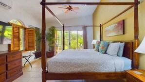 A four-poster bed with a ceiling fan, a television, and a view of greenery outside. - Casa Tropical, Spacious 3 BR Home with Pool (Brasilito)
