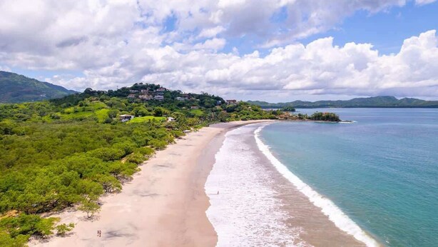 A coastal landscape with a beach, a small island, and a hill with buildings. - Casa Tropical, Spacious 3 BR Home with Pool (Brasilito)