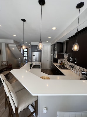 Una cocina moderna con una isla central, armarios oscuros e iluminación colgante.