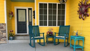 A porch with two rocking chairs, a small table, and a decorative wall piece.