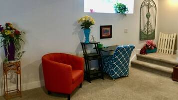 Una habitación con un sillón rojo, una silla azul estampada, una mesita y una pared blanca con una verja decorativa de metal.