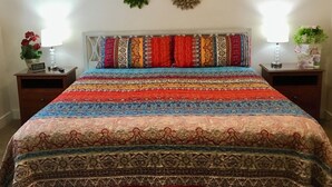 A bedroom with a colorful striped bedspread, a patterned headboard, and decorative wall hangings.