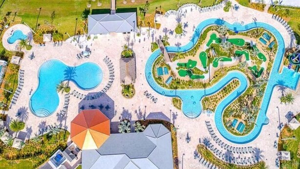 Oversigtsbillede af et resort med flere swimmingpools, en stor parasolstruktur og et snoet vandelement.