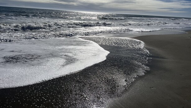 Een strand met golven die op de kust breken onder een heldere lucht.