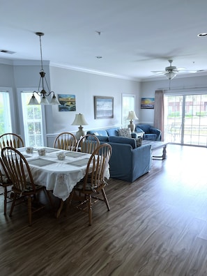 Un coin repas avec une table dressée pour quatre personnes, des chaises en bois et un canapé bleu en arrière-plan.